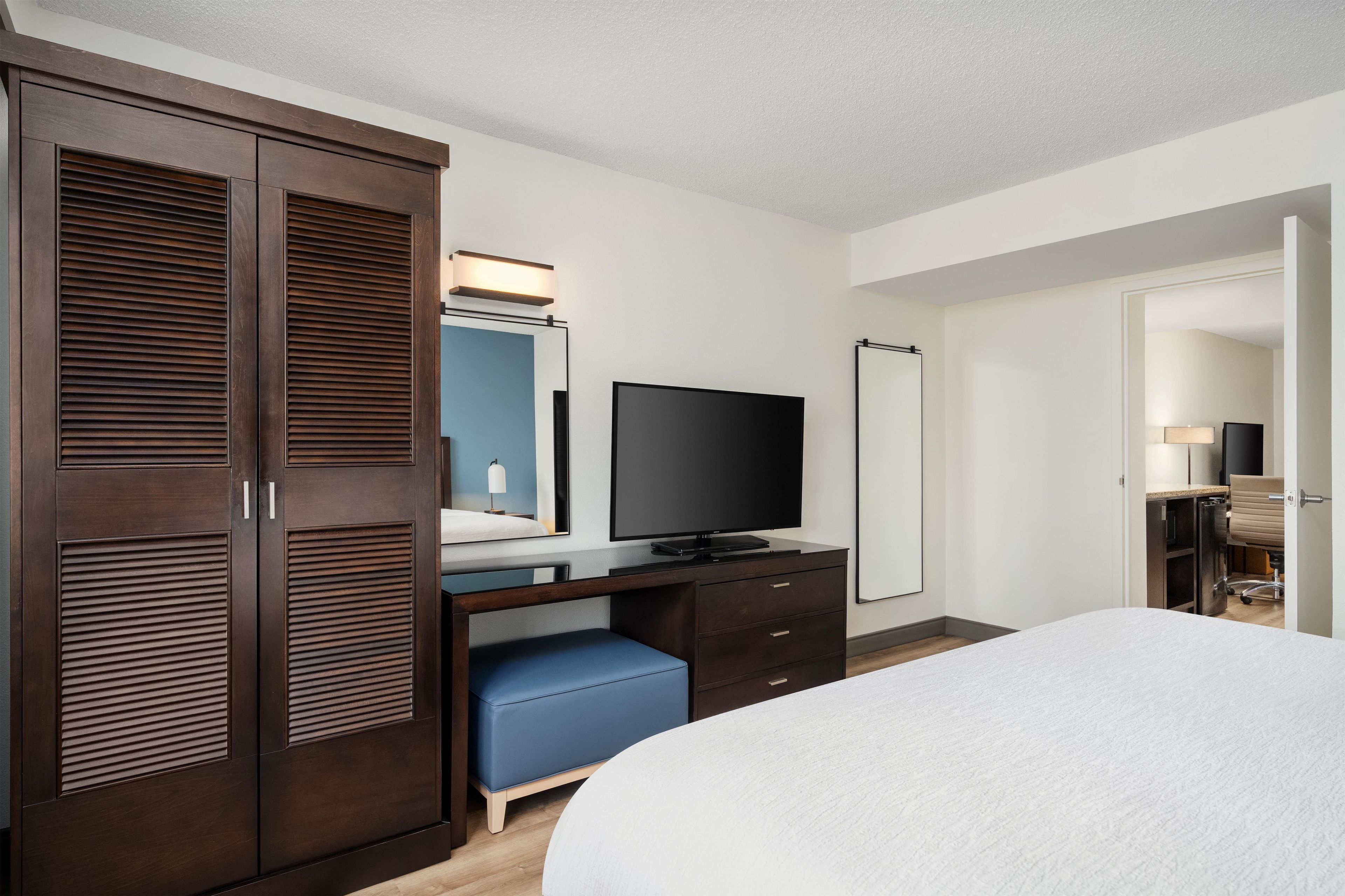 A hotel room with a bed, a desk with a flat-screen TV, a wardrobe, and a mirror.