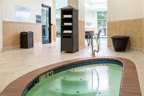 A pool area with a hot tub, a trash can, and a towel rack.