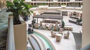 Een ruime, overdekte lobby met diverse zithoeken, een centrale waterpartij en een hoge plafond.
