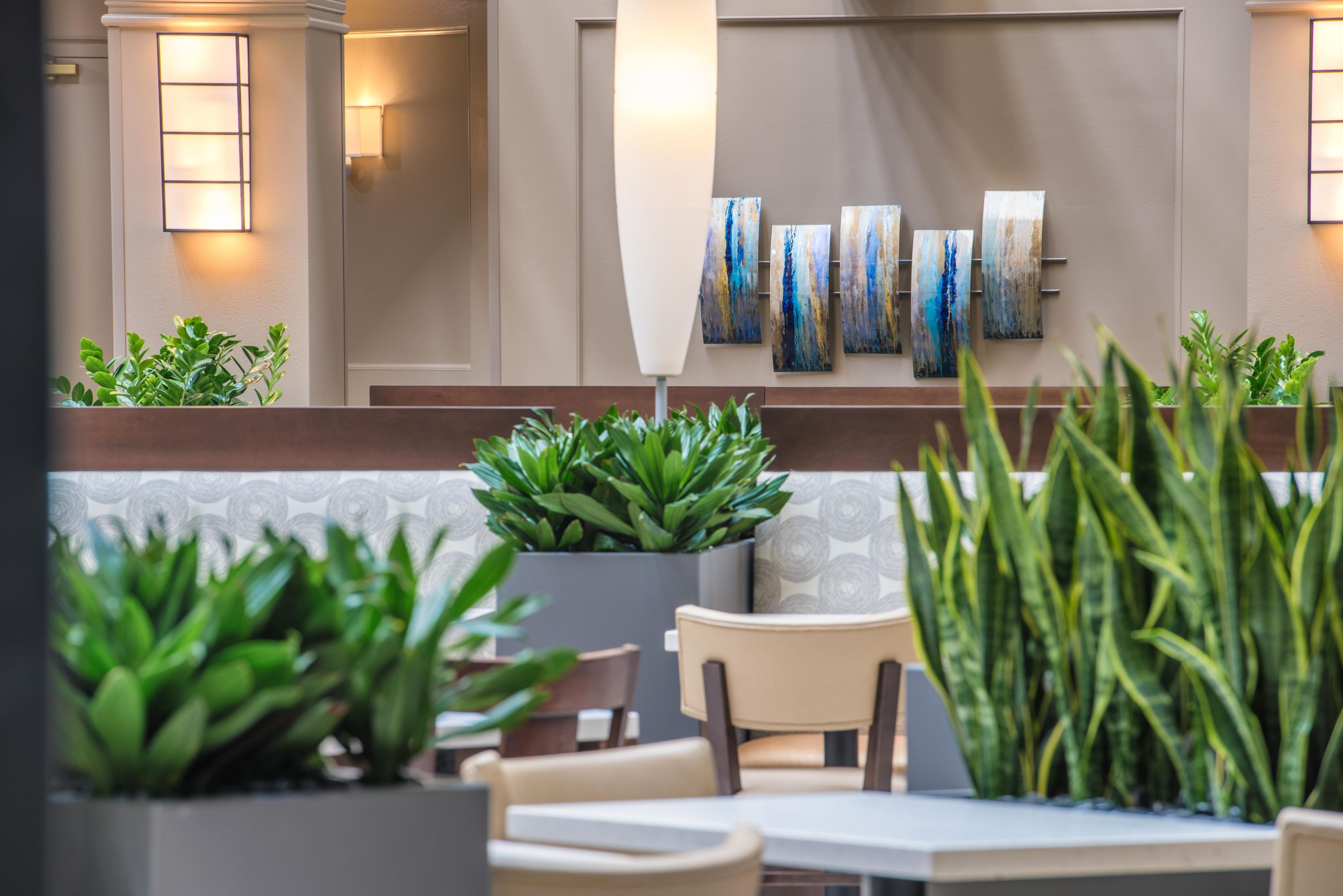 A hotel lobby with a seating area, potted plants, and wall art.