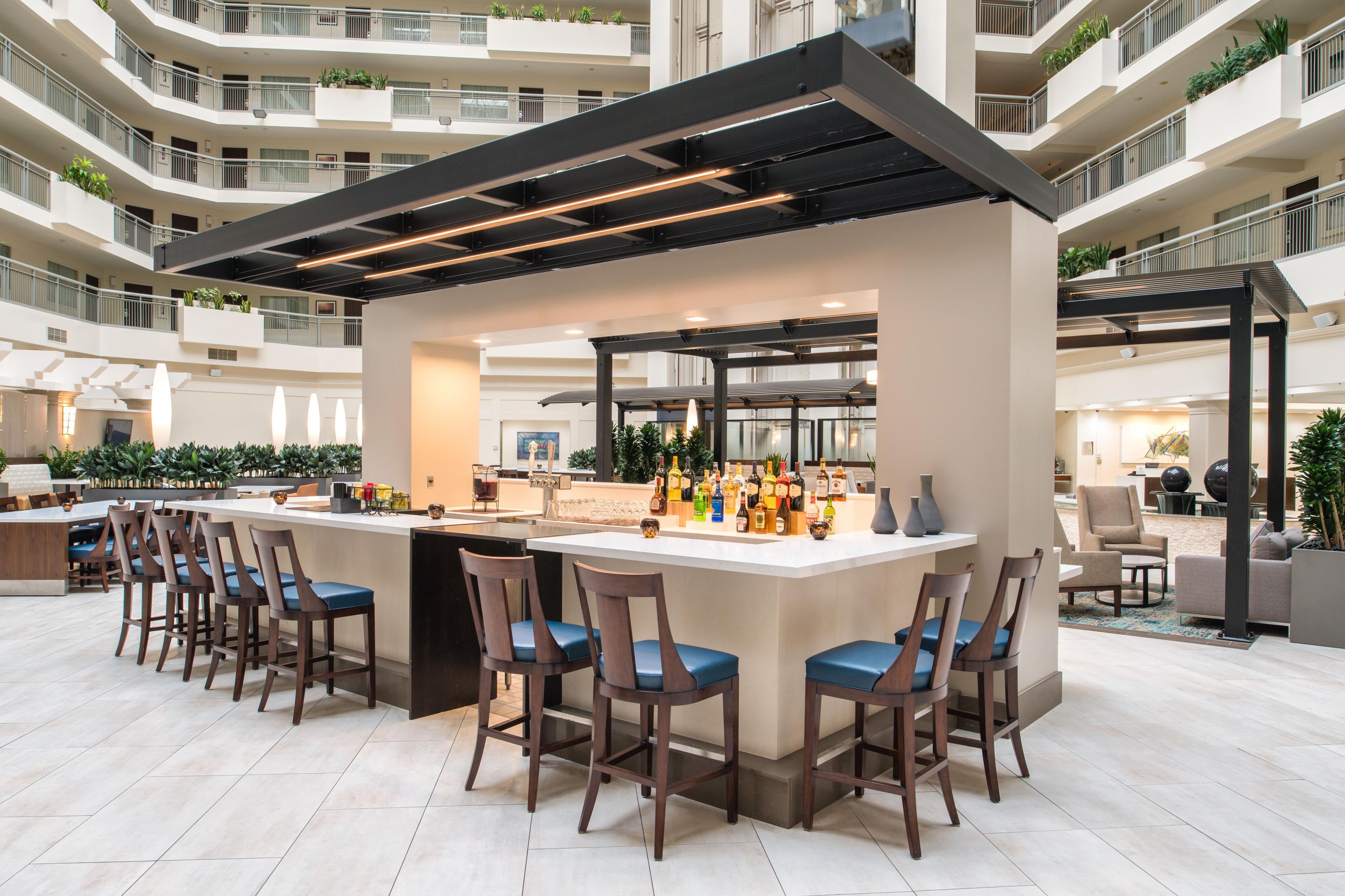 Un bar moderno con una barra central, diversas opciones de asientos y vistas al interior del edificio circundante.