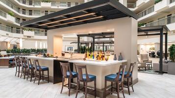 Un bar moderno con una barra central, diversas opciones de asientos y vistas al interior del edificio circundante.