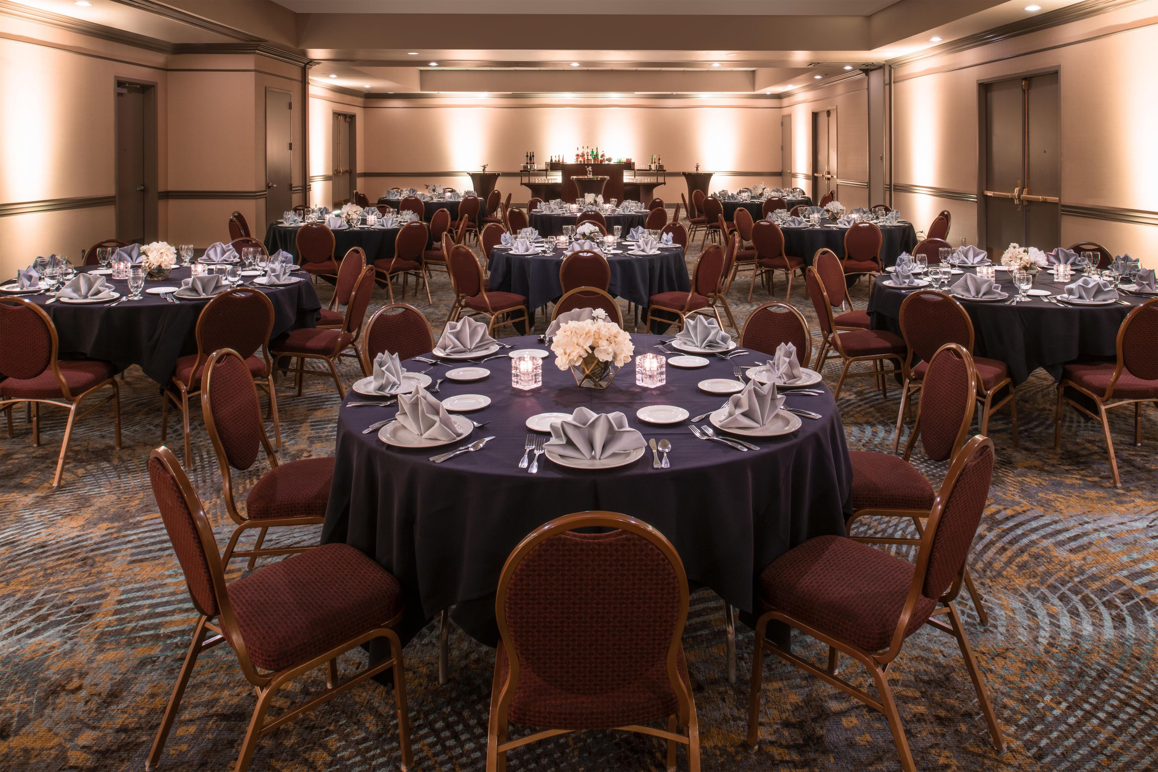 Un salón de conferencias con mesas redondas, sillas y una zona de bar.