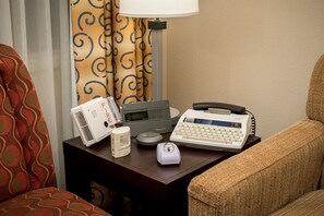 Habitación de hotel con un escritorio que presenta una máquina de escribir antigua, un proyector moderno y un pequeño altavoz.
