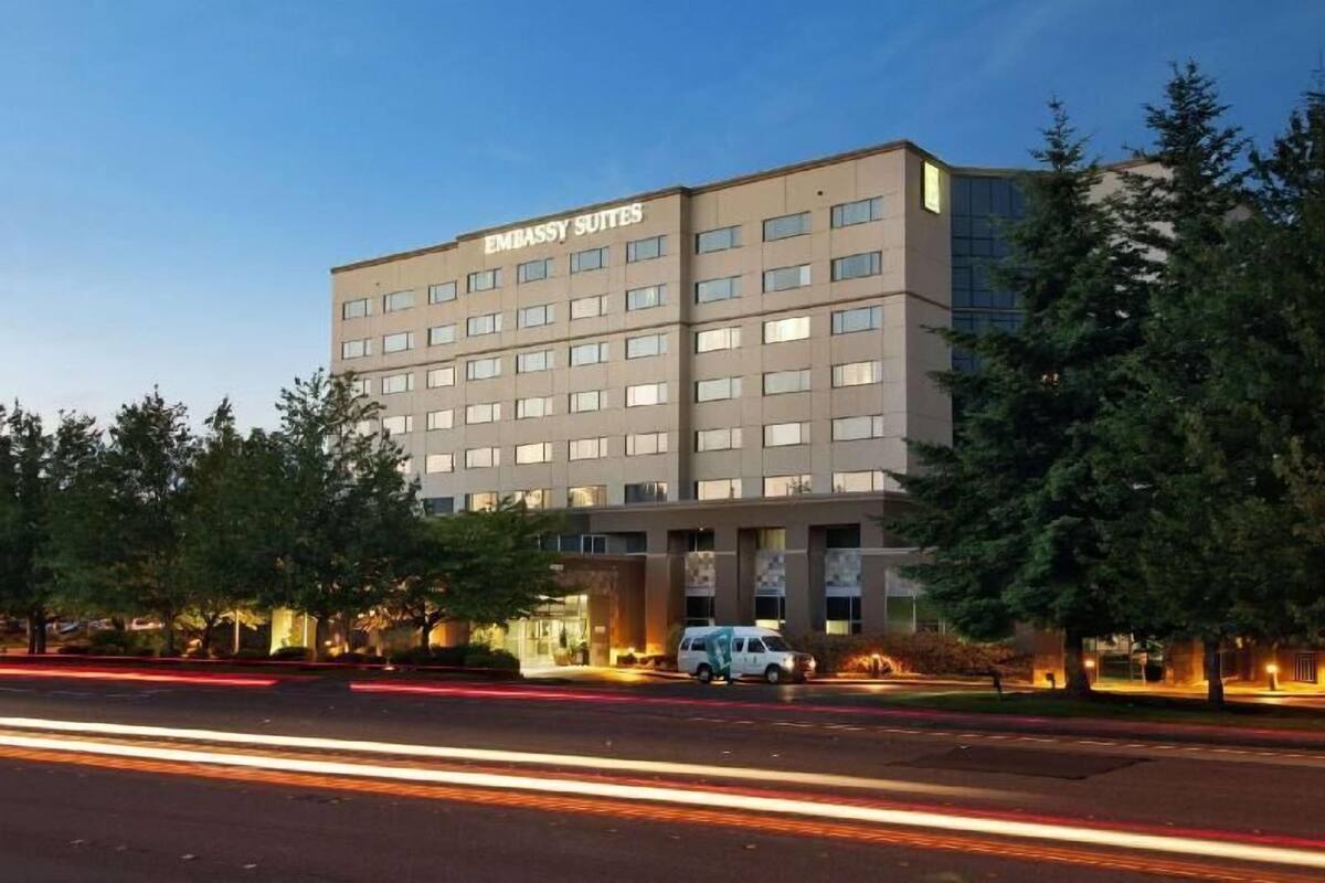A multi-story building with 'EMBASSY SUITES' signage, a parking area, and a road with light trails.