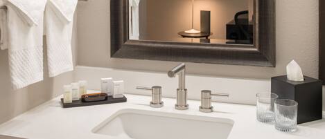 A modern bathroom with a white sink, two faucets, a mirror, and a towel rack.