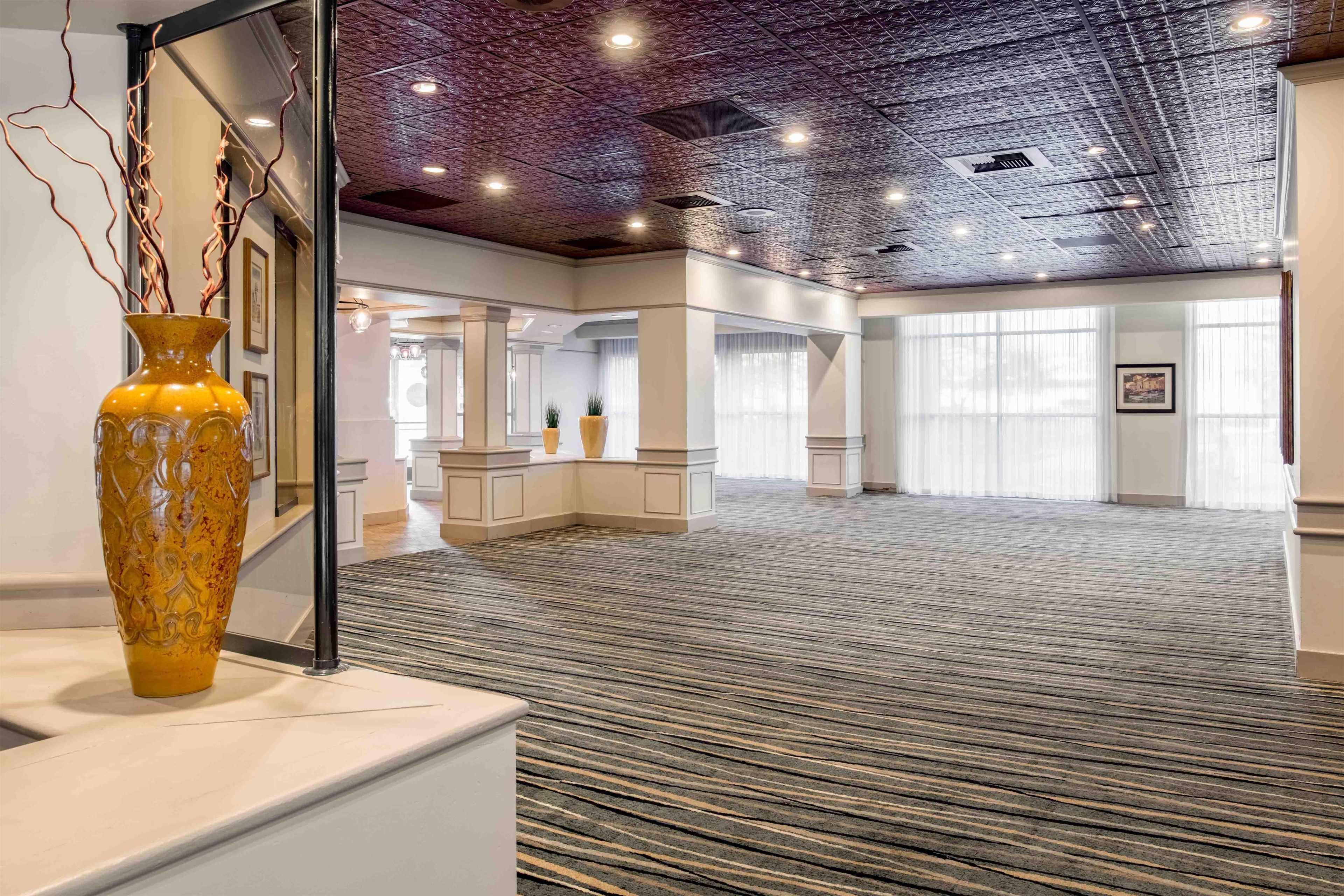 A spacious hotel lobby with a patterned carpet, a reception desk, and a large window with curtains.