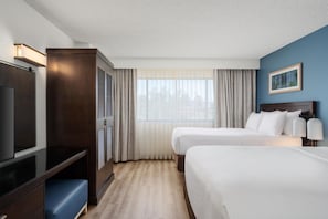 A hotel room with a TV, two beds, a desk, and a window with curtains.