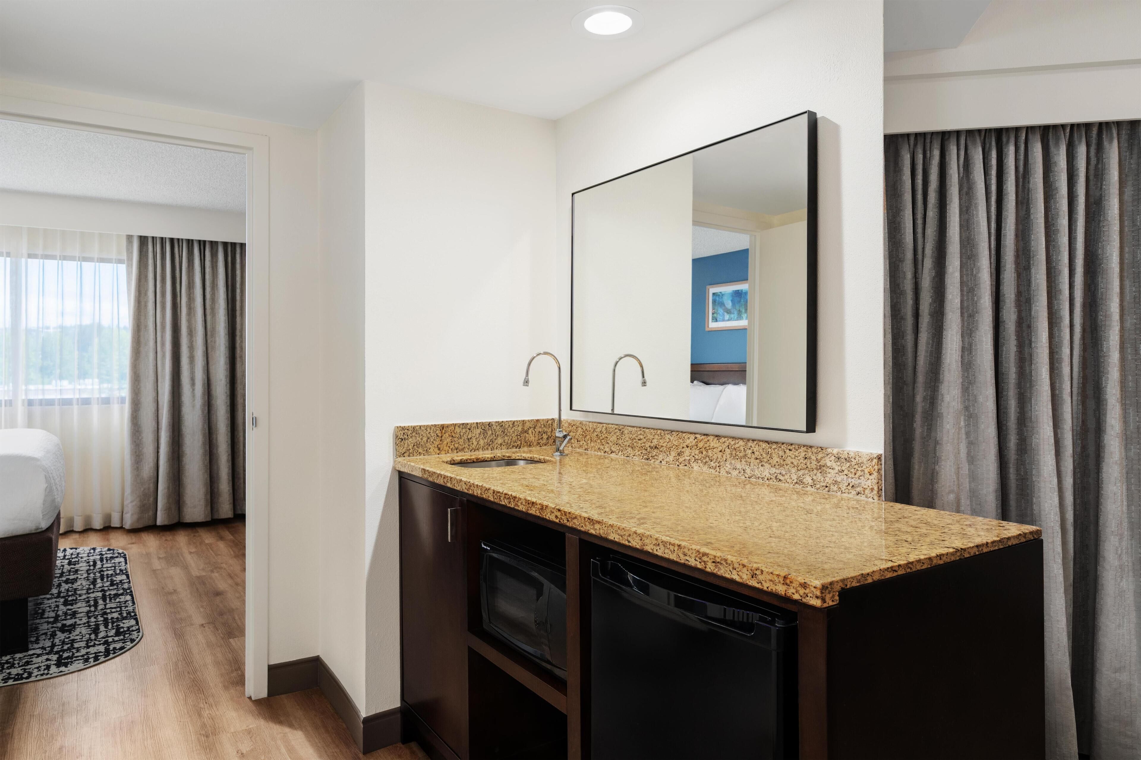 Une salle de bain moderne avec un comptoir en granit, un lavabo, un miroir et un meuble sombre.