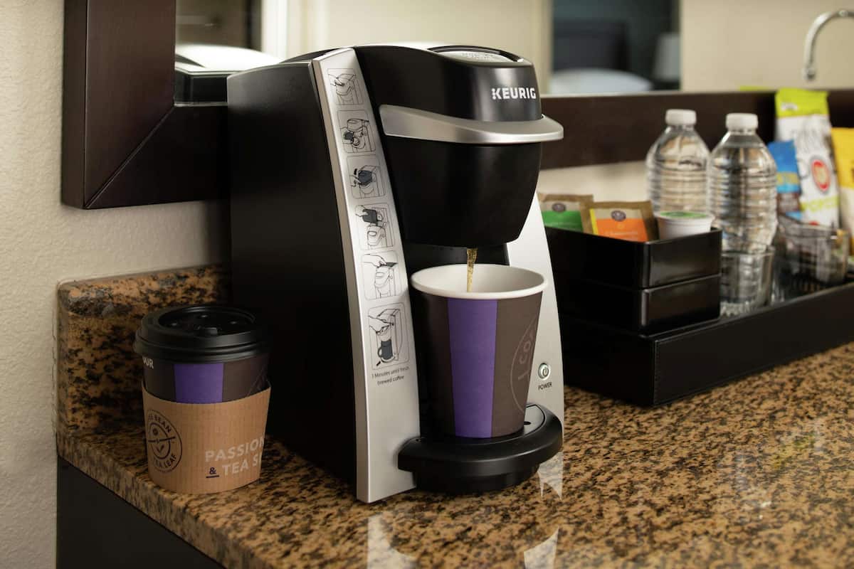 A Keurig coffee maker with a drip tray, a disposable cup, and a water bottle on a granite countertop.