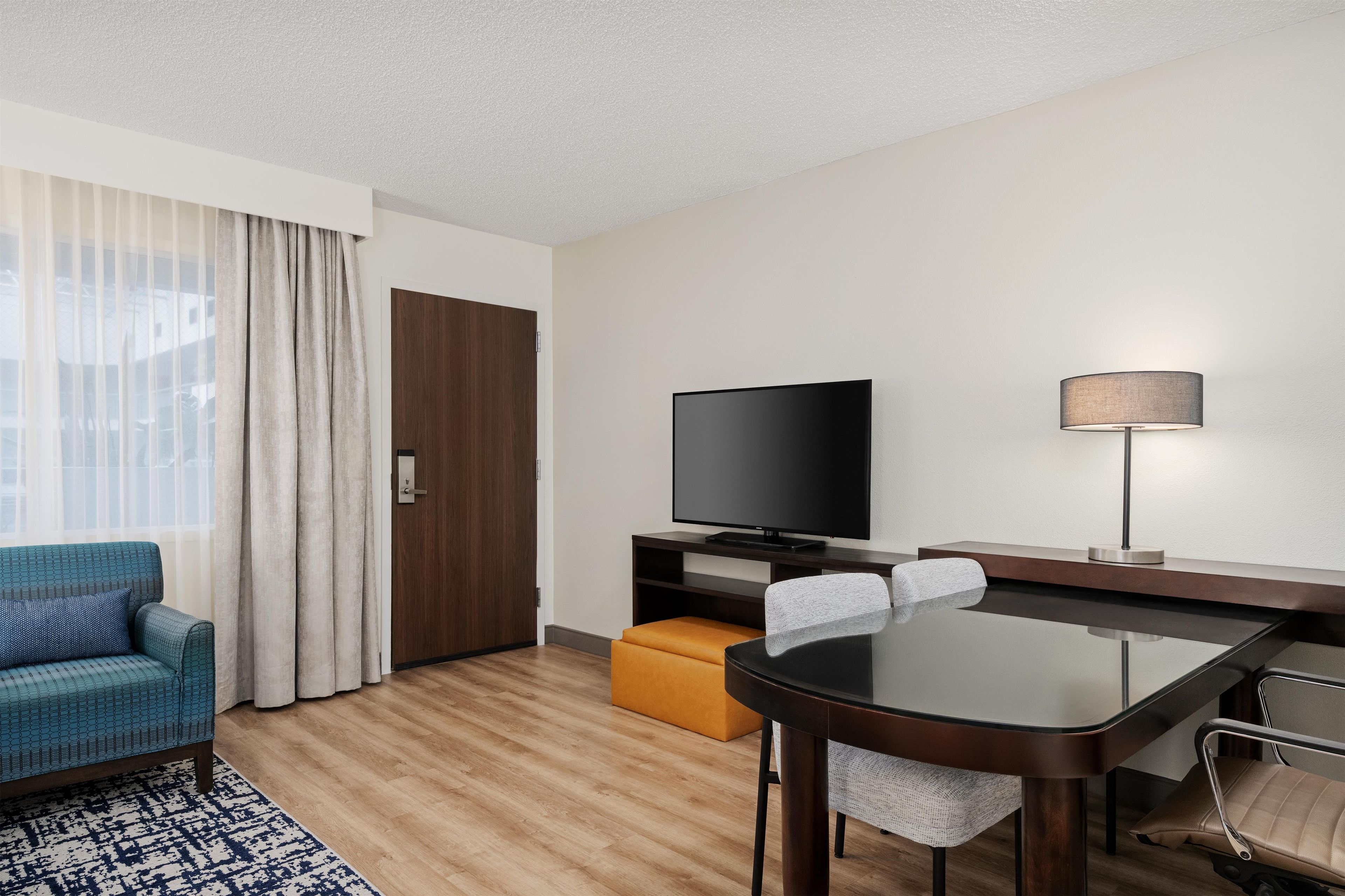 A modern hotel room with a sofa, a television, a dining table, and a lamp.