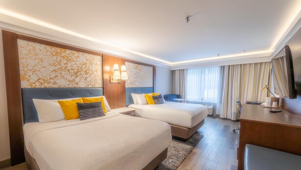Une chambre d’hôtel avec deux lits, un bureau, une télévision et une grande fenêtre avec des rideaux.