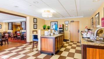 Un hall de hotel con piso a cuadros, una recepción, una estación de café y un comedor con sillas y mesas.