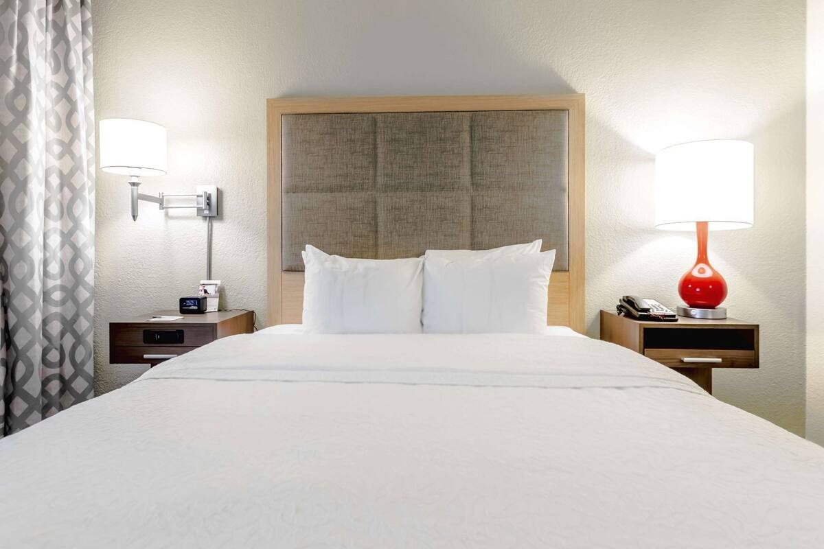 A hotel room with a large bed, two bedside tables, a red lamp, and a wall-mounted lamp.