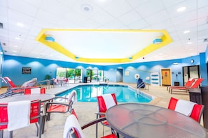 A swimming pool area with red and white lounge chairs, a glass table, and a blue and yellow ceiling.