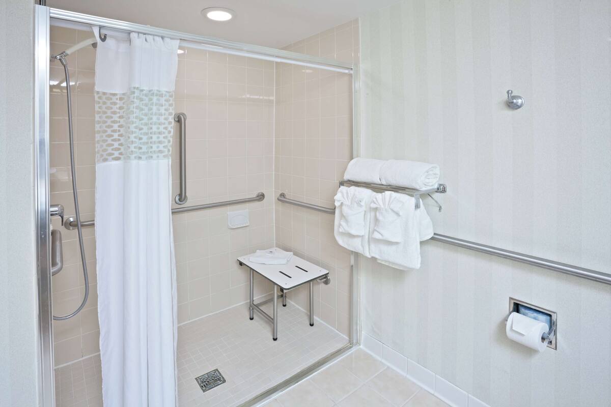 A modern bathroom with a glass shower enclosure, a small table, a towel rack, and a toilet paper holder.