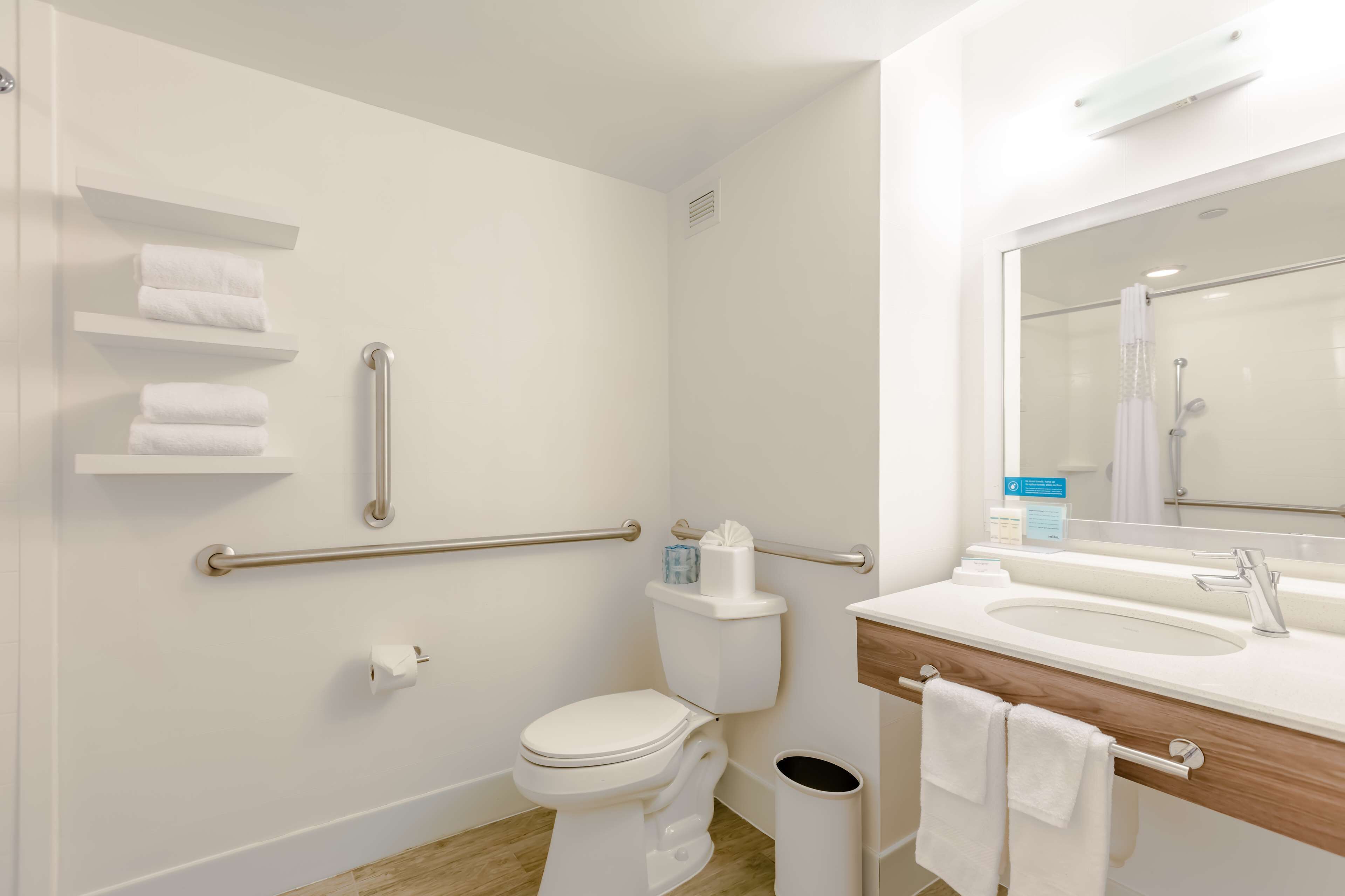 A modern bathroom with a toilet, handrails, a sink, and a mirror.