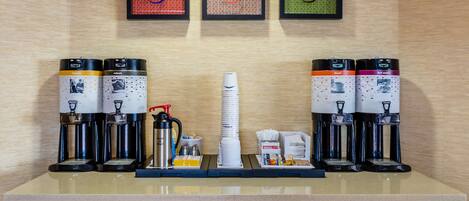 A coffee station with multiple coffee makers and a stack of disposable cups.
