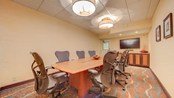 A conference room with a long table, six chairs, a TV, and a carpeted floor.
