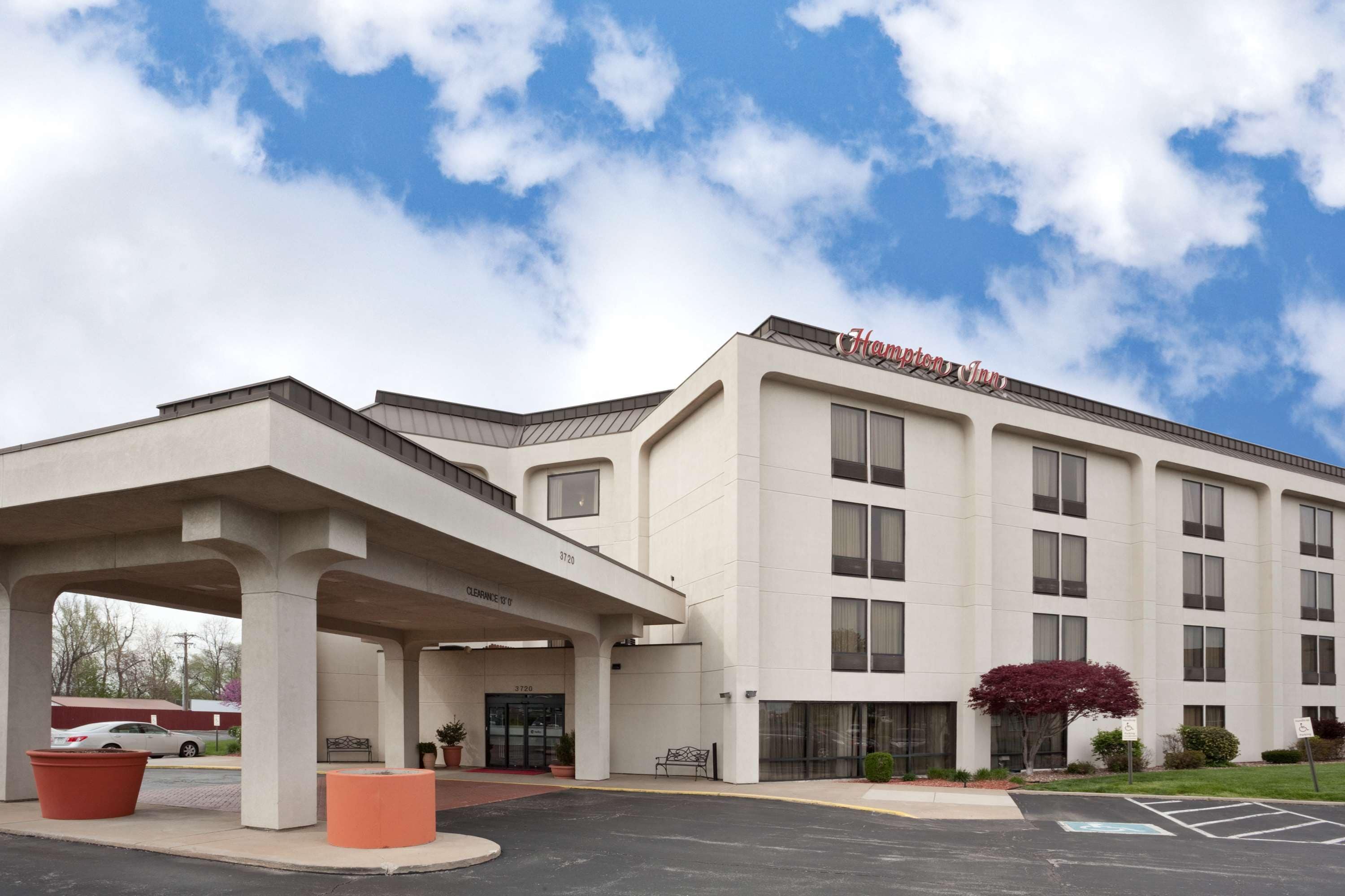 A hotel with a modern design, featuring a covered entrance, a large parking area, and a clear sky.