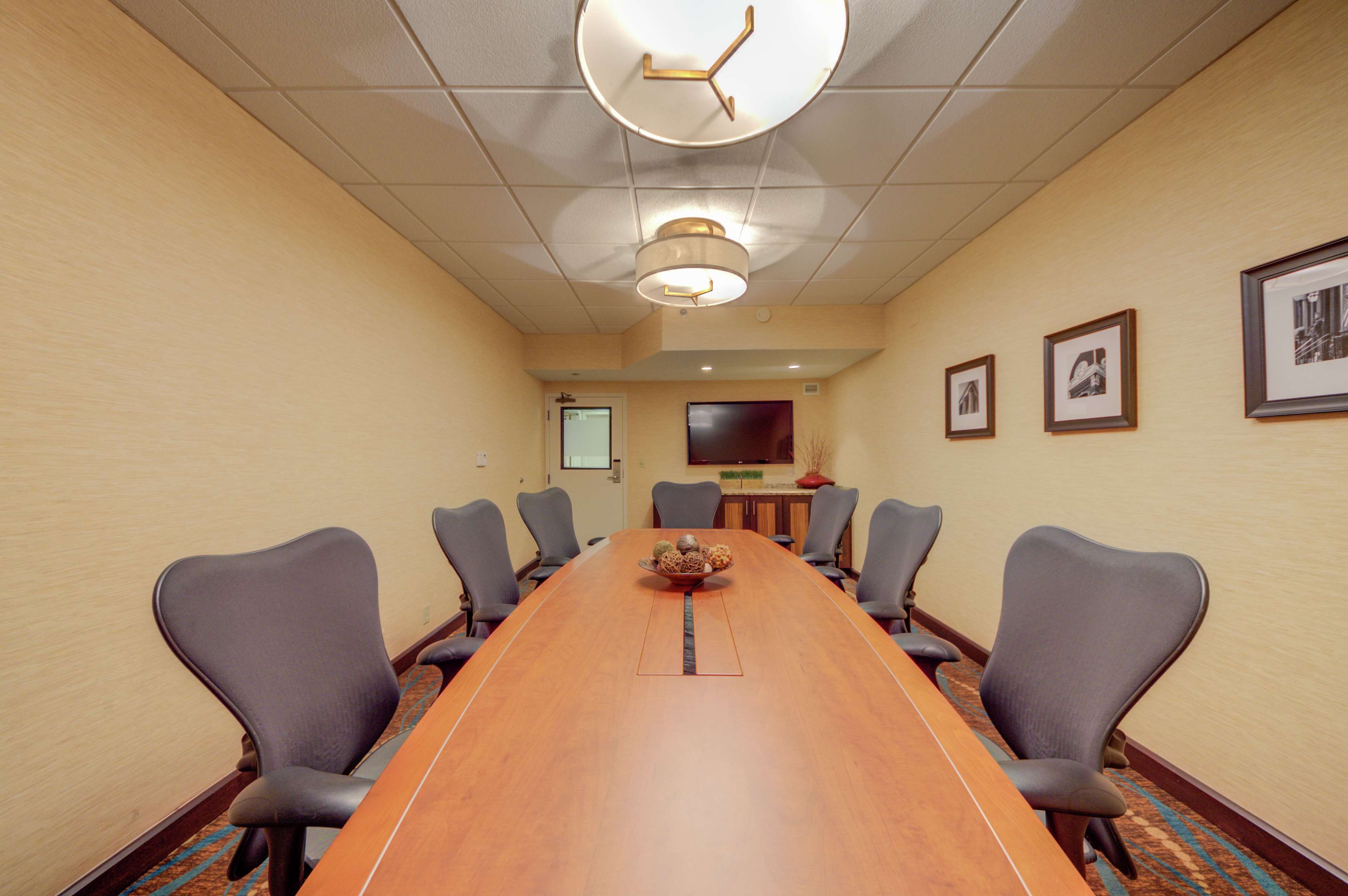 A conference room with a long table, six chairs, a clock, and framed pictures on the wall.