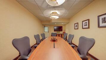A conference room with a long table, six chairs, a clock, and framed pictures on the wall.