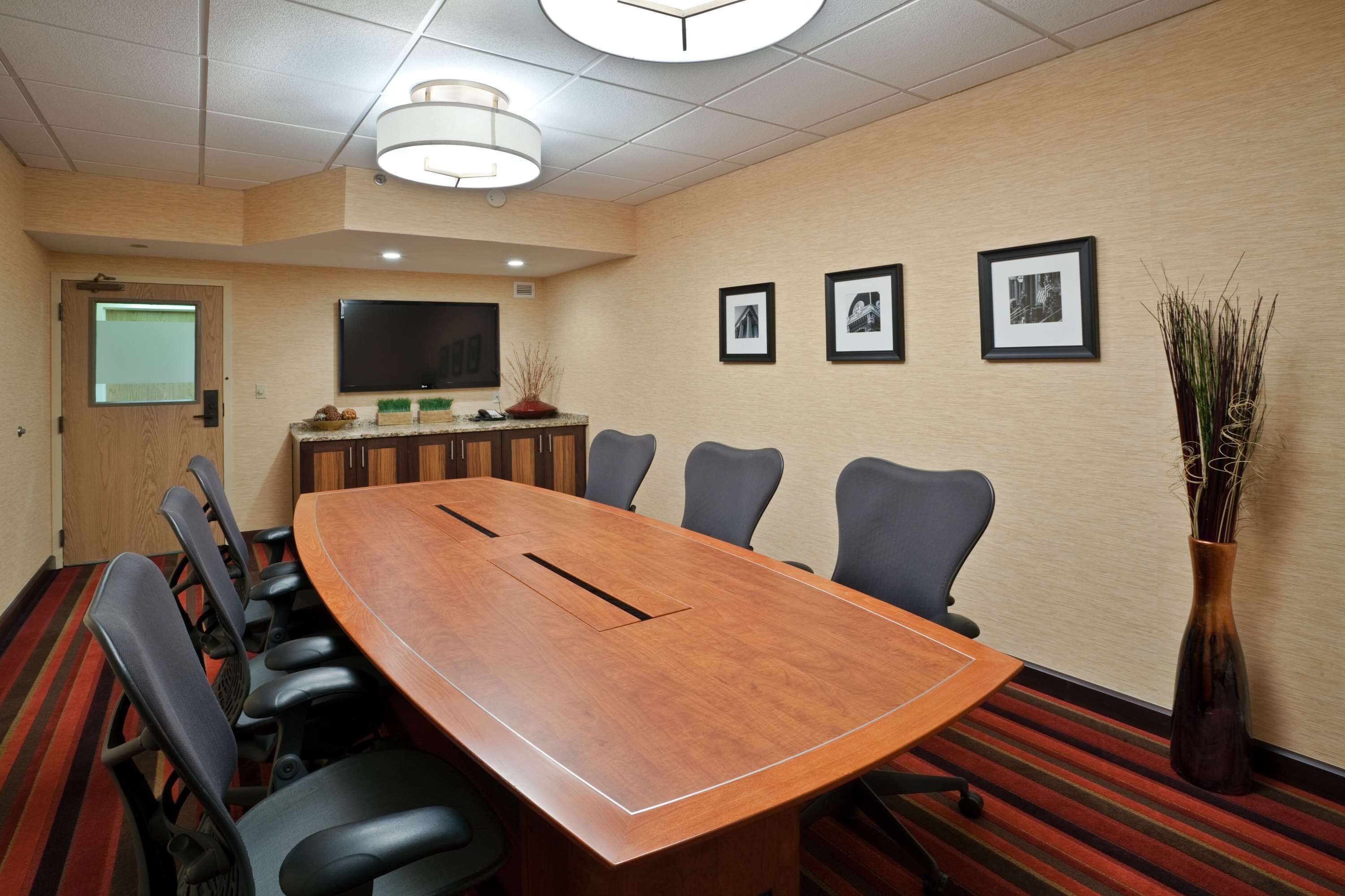 A conference room with a long table, six chairs, a flat-screen TV, and framed pictures on the wall.