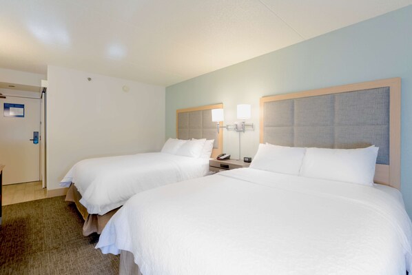 A hotel room with two beds, a nightstand, a lamp, and a door.