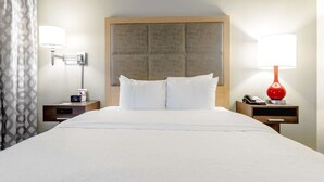 A hotel room with a large bed, two bedside tables with lamps, a headboard, and a curtain.