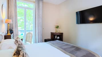 Une chambre d’hôtel avec un lit, un téléviseur fixé au mur, un bureau avec une lampe et une vue sur la verdure à l’extérieur.