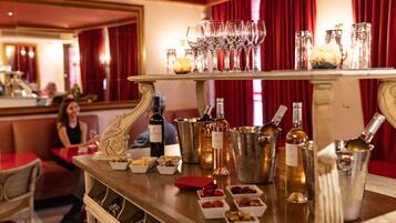 Uma área de bar com seleção de vinhos e cocktails, copos e pequenas porções de petiscos.