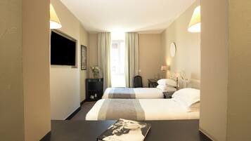Een hotelkamer met twee bedden, een flatscreen televisie, een nachtkastje met een boek en een raam met gordijnen.