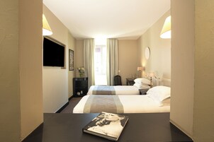 Een hotelkamer met twee bedden, een flatscreen televisie, een nachtkastje met een boek en een raam met gordijnen.