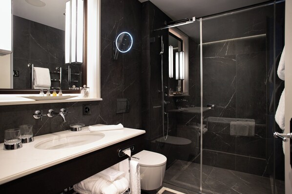 A modern bathroom with a large mirror, a glass-enclosed shower, and a white sink.