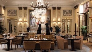 A luxurious hotel lobby with a grand chandelier, elegant seating arrangements, and a large decorative painting on the wall.