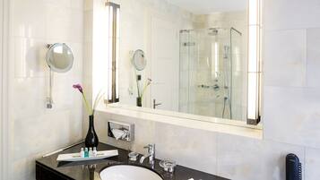 Une salle de bain moderne avec un grand miroir, un meuble-lavabo rond, une douche en verre et un téléphone.