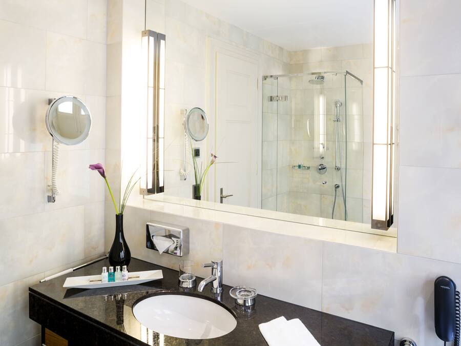 Une salle de bain moderne avec un grand miroir, un meuble-lavabo rond, une douche en verre et un téléphone.