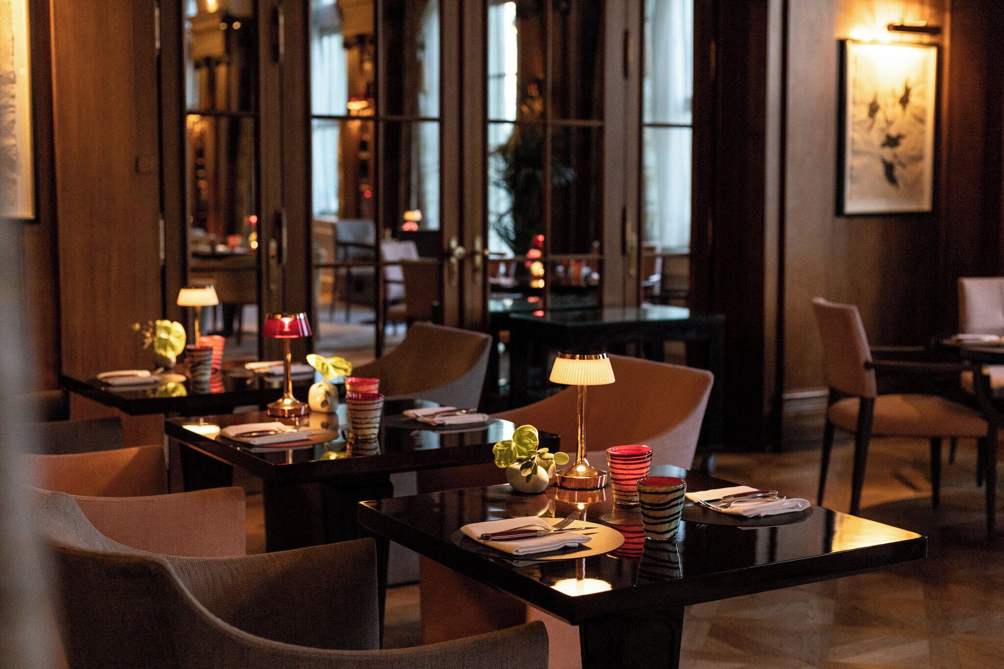 Un comedor bien iluminado con mesas dispuestas para dos, con decoración moderna e iluminación ambiental.