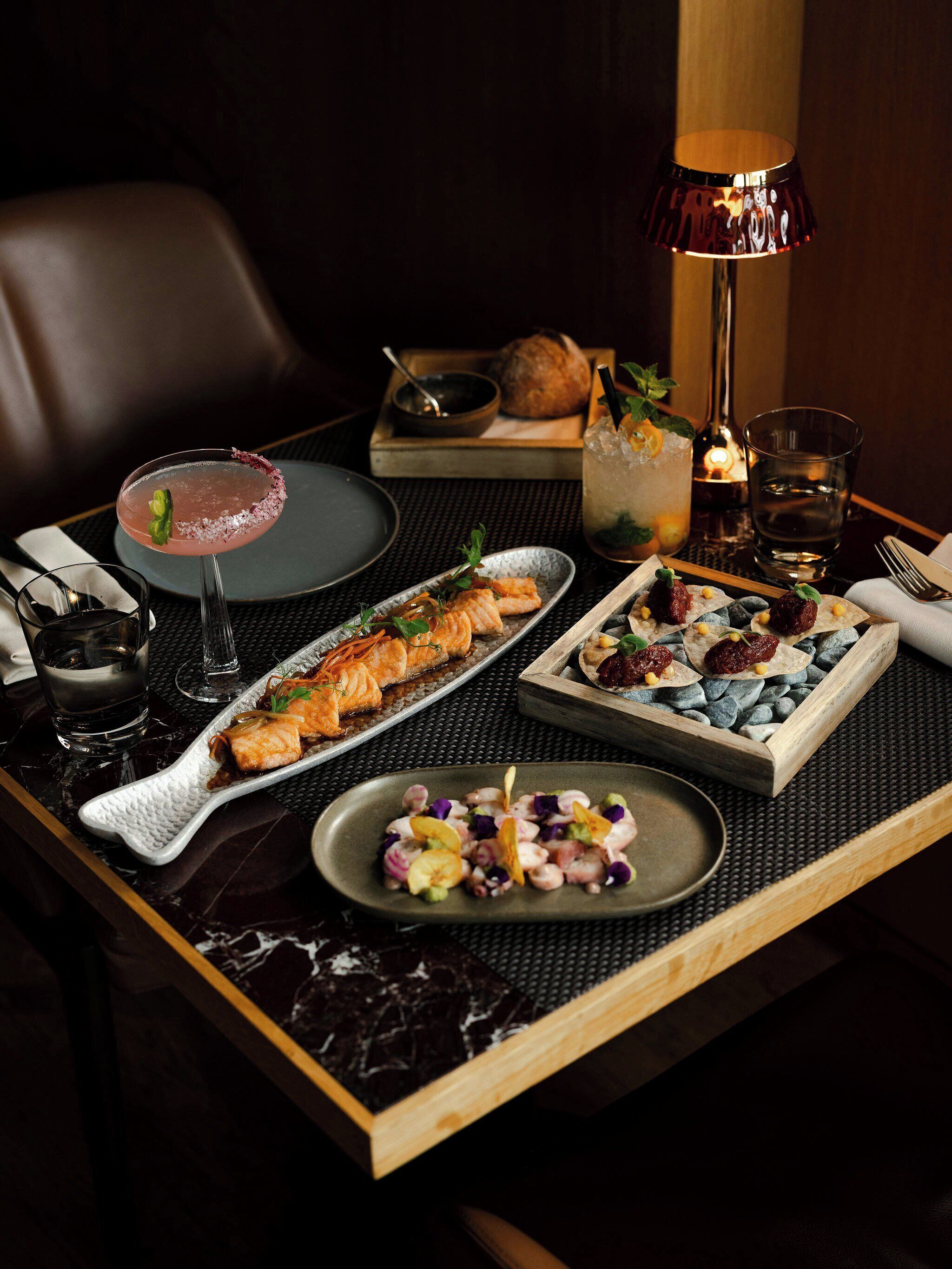 A dining table with a variety of dishes, a cocktail, and a candle.