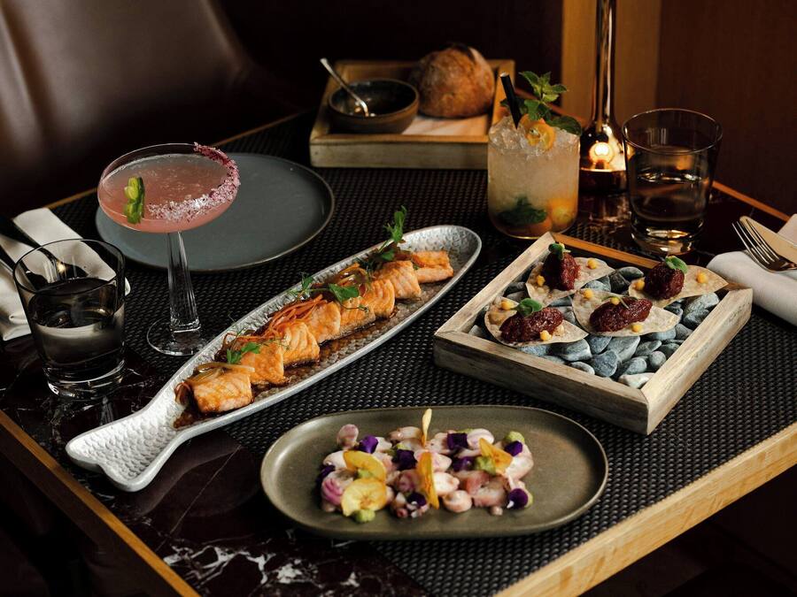A dining table with a variety of dishes, a cocktail, and a candle.