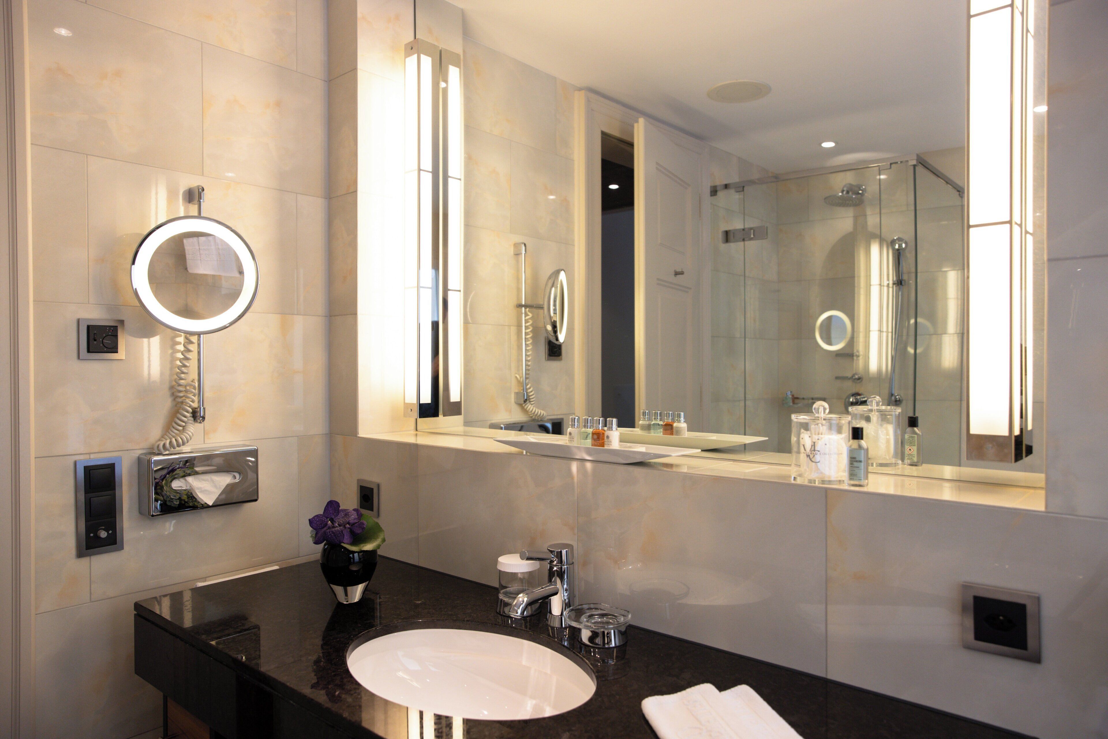 Un baño moderno con un espejo grande, un lavamanos y una ducha con mampara de vidrio.
