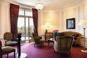 A room with a glass table, two armchairs, a sofa, a wooden cabinet, and a chandelier.