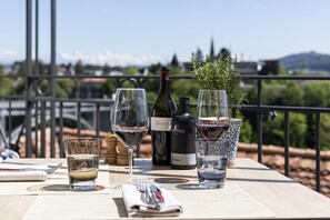 Mesa dispuesta con copas de vino, una botella y una pequeña planta en una terraza con vistas al campo.