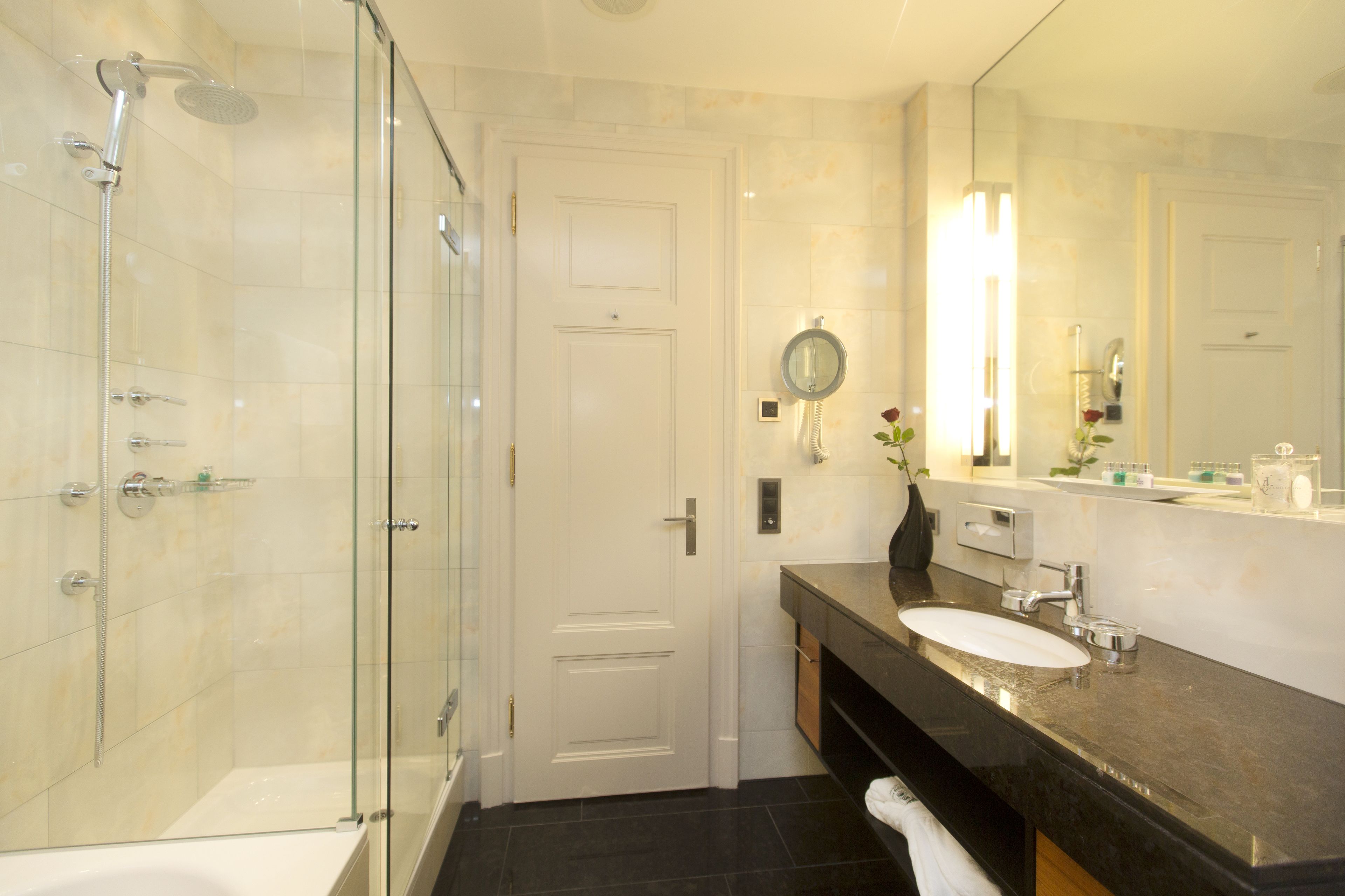 Une salle de bain moderne avec une douche à parois de verre, une baignoire blanche, un grand miroir et un lavabo sur un plan de toilette foncé.