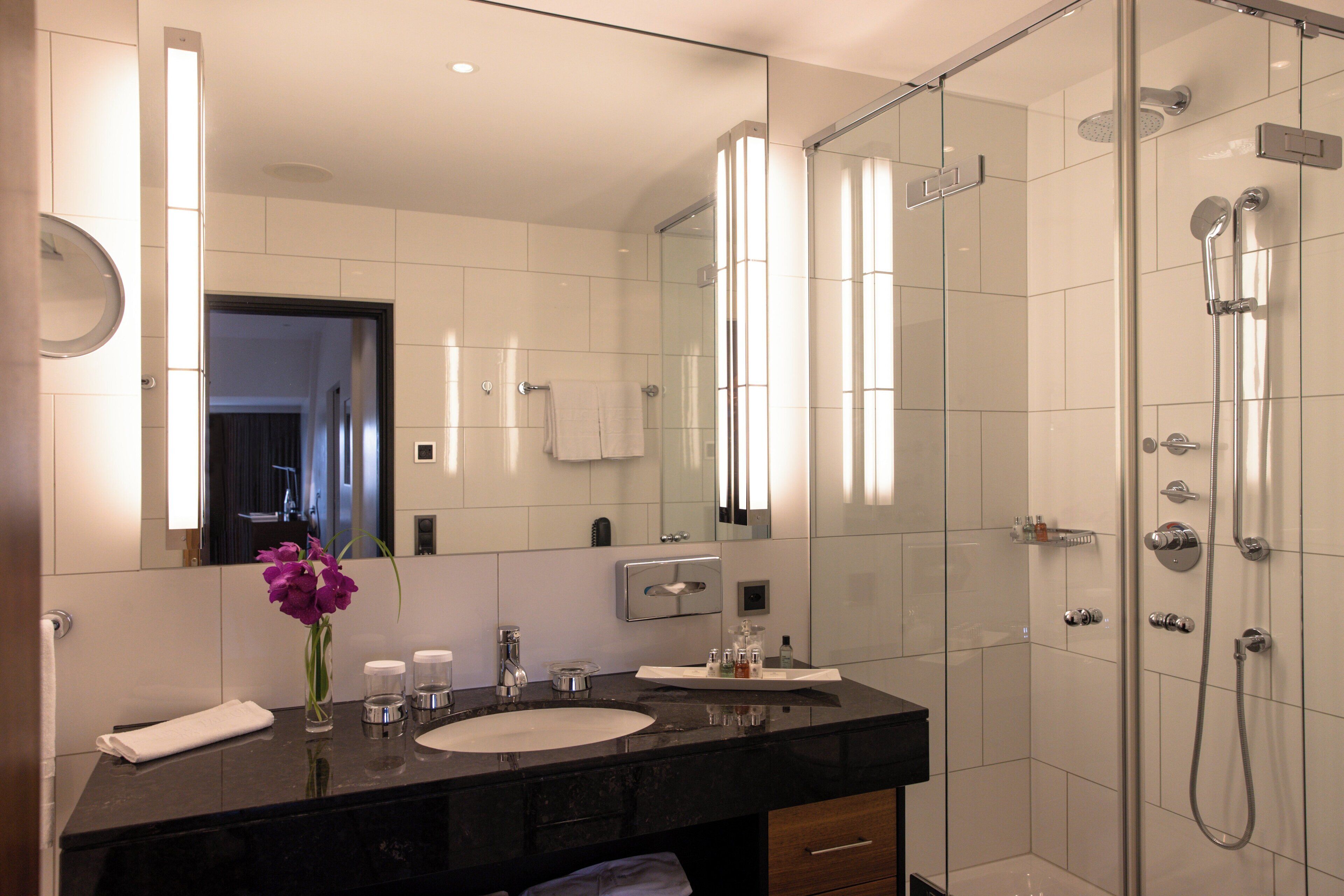 A modern bathroom with a black countertop, white sink, and a glass-enclosed shower.