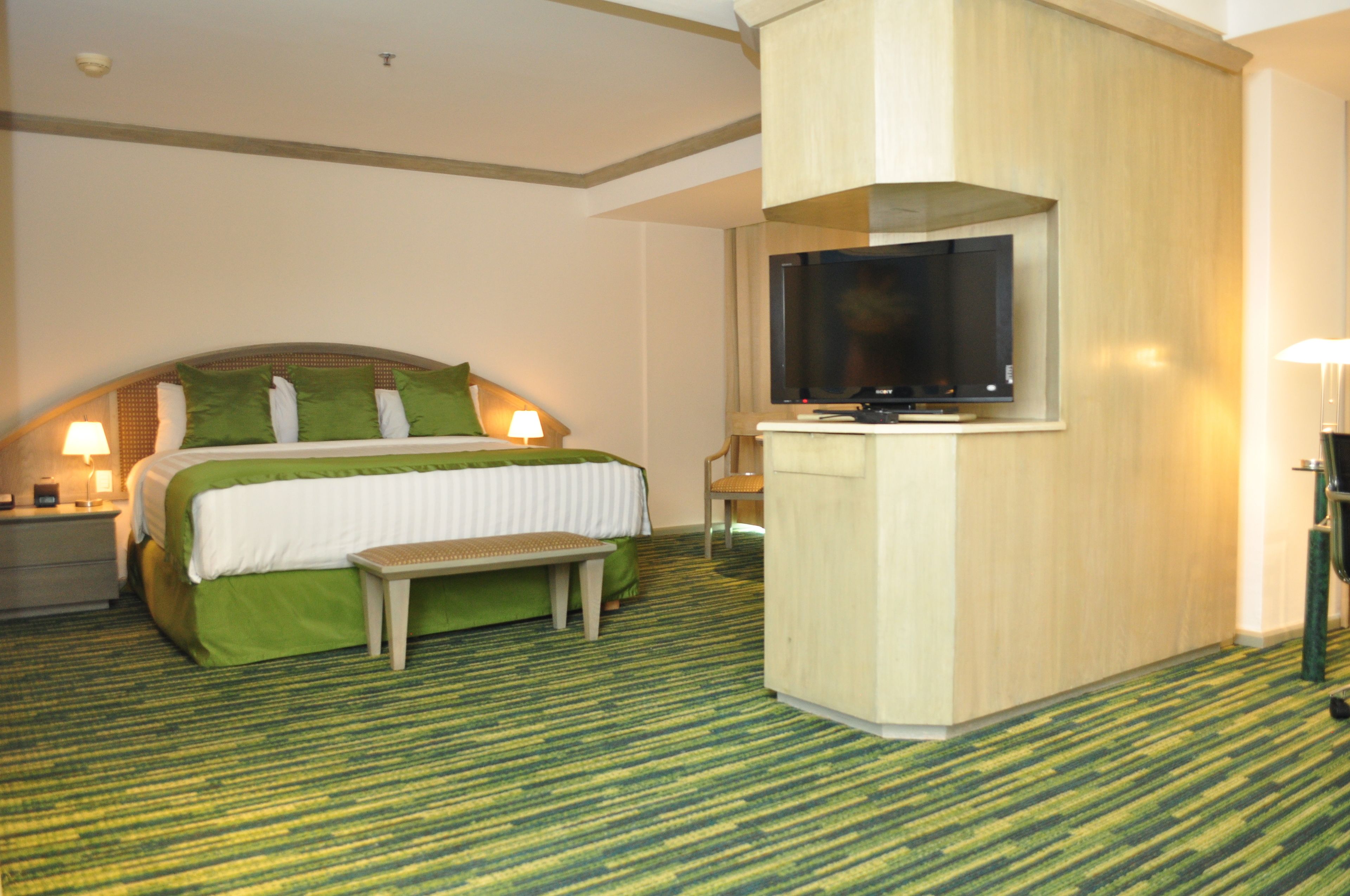 Quarto de hotel com cama, um banco, televisão e escrivaninha.