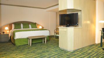 Quarto de hotel com cama, um banco, televisão e escrivaninha.