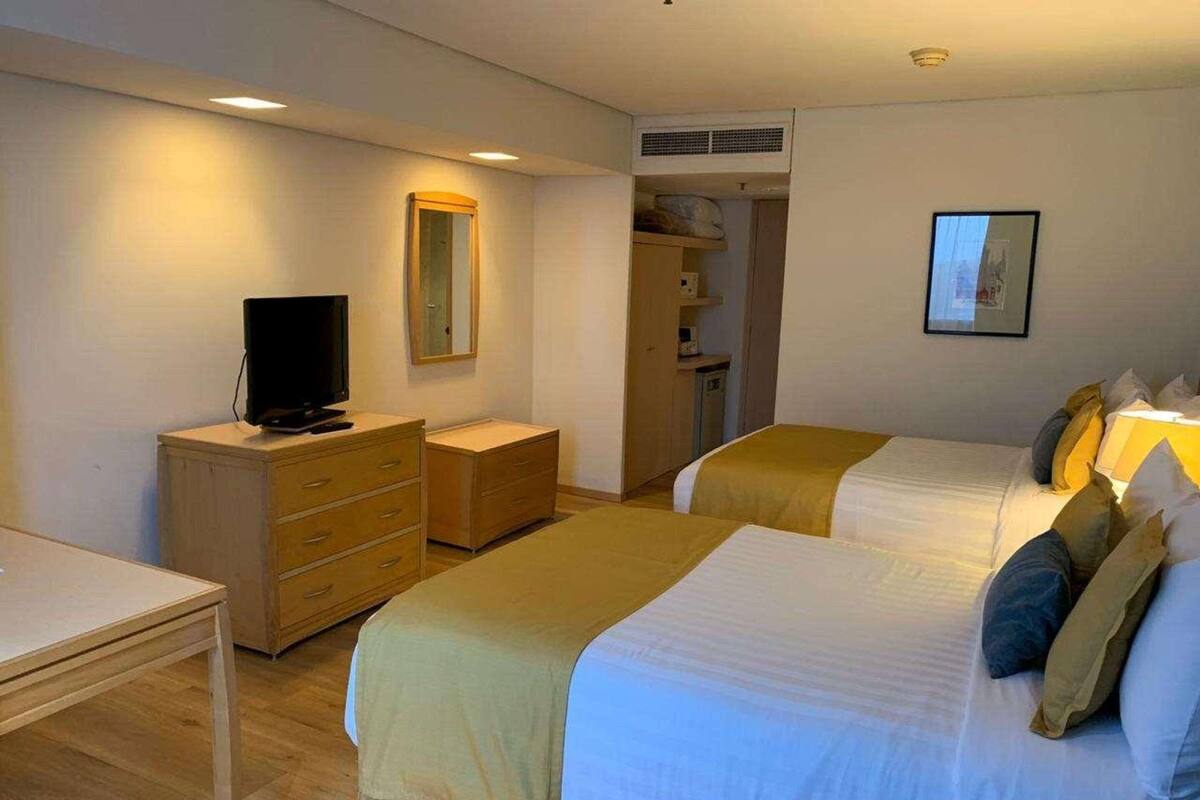 A hotel room with two beds, a TV, a wardrobe, and a small desk.