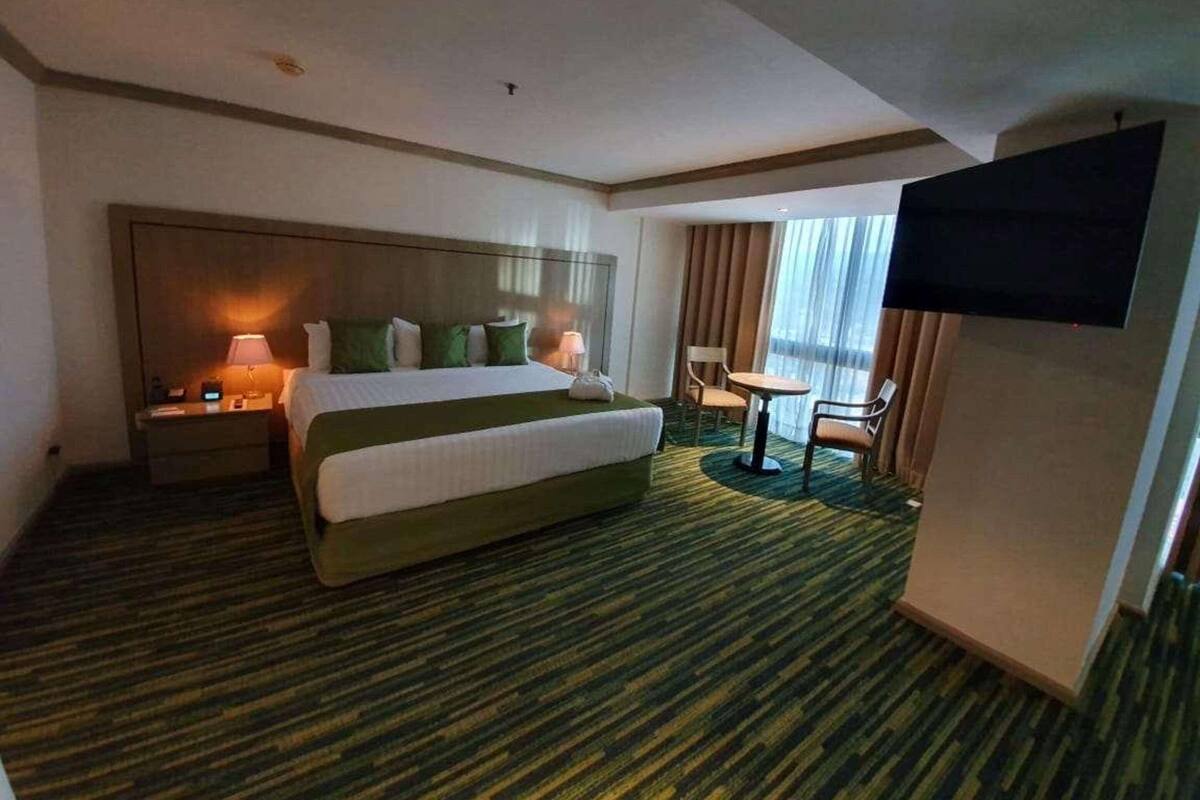 A hotel room with a large bed, a desk with a chair, a television, and a window with curtains.