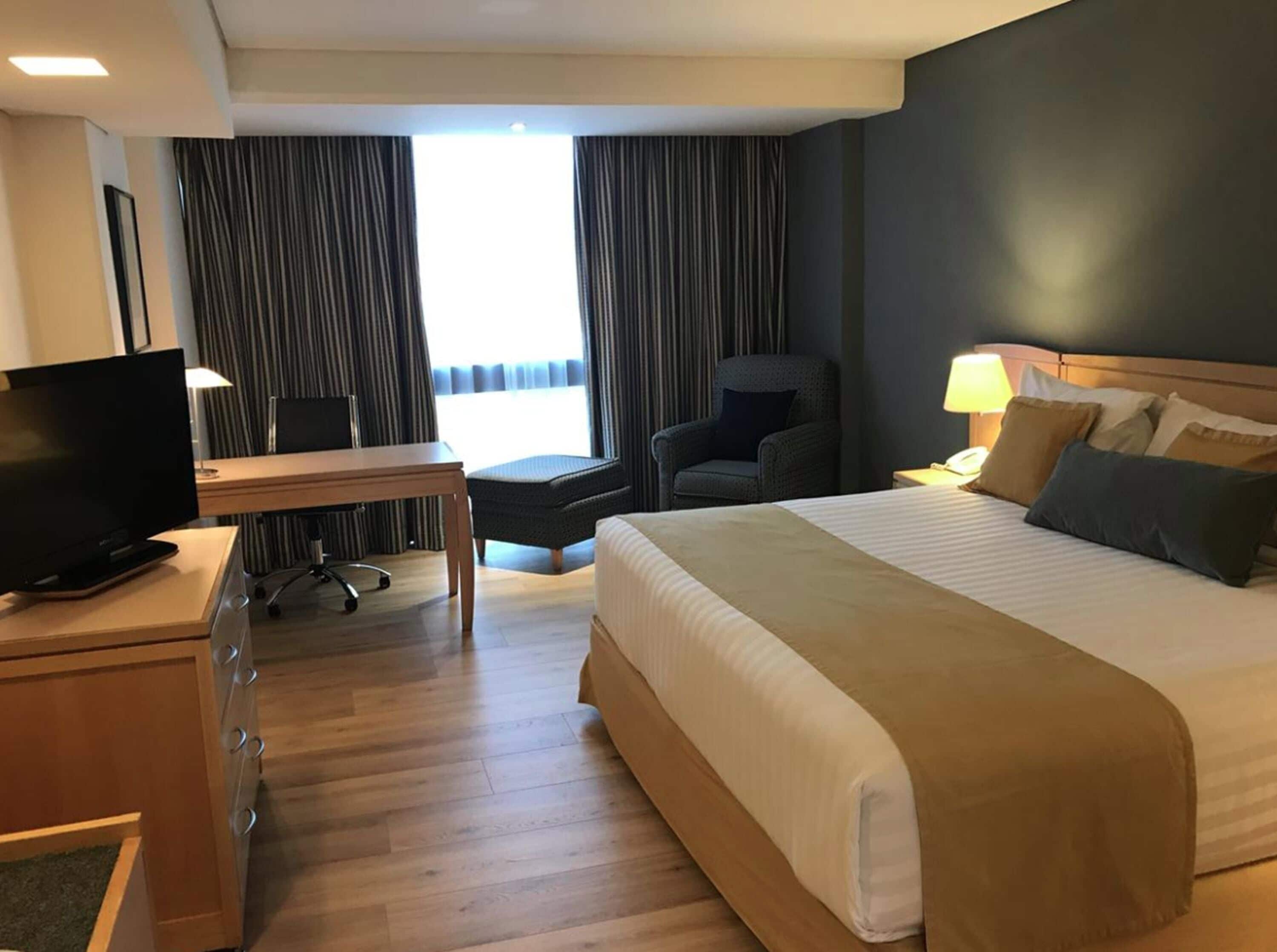 A hotel room with a bed, a desk with a computer, a chair, and a TV.
